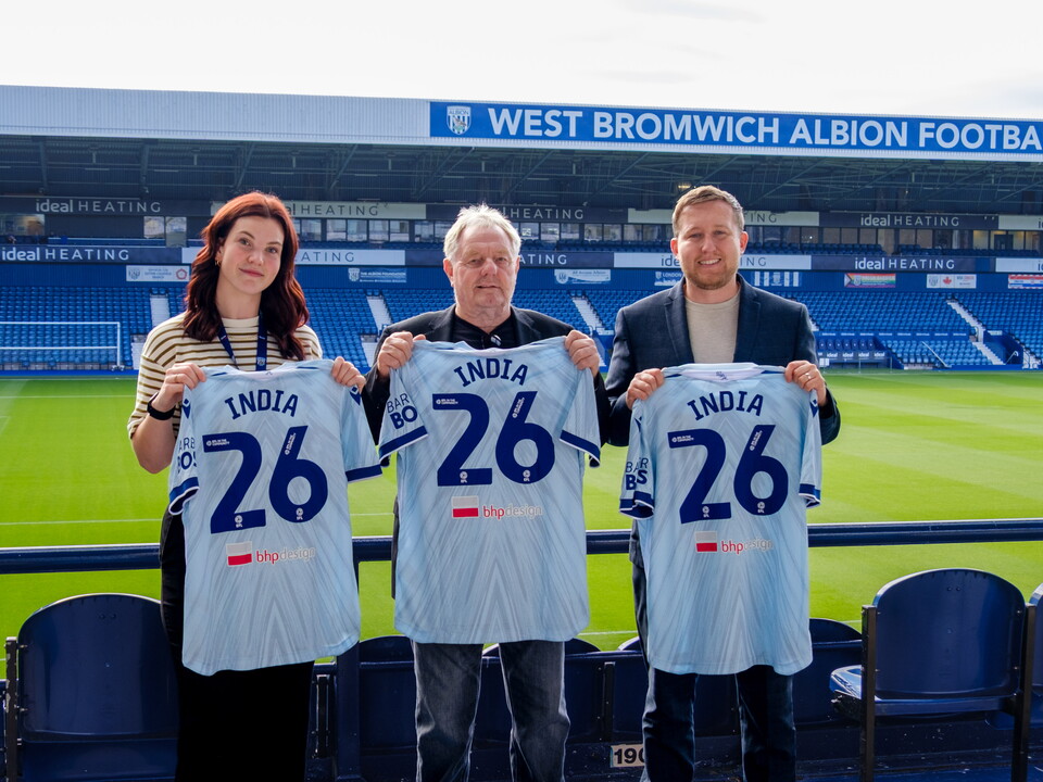 Dave Bloxham, of BHP Design (centre) with Sophie Osbourne (left) and Jonathan Ward, Deputy Director (right) all holding WBA third kit shirts with India 26 on the back.